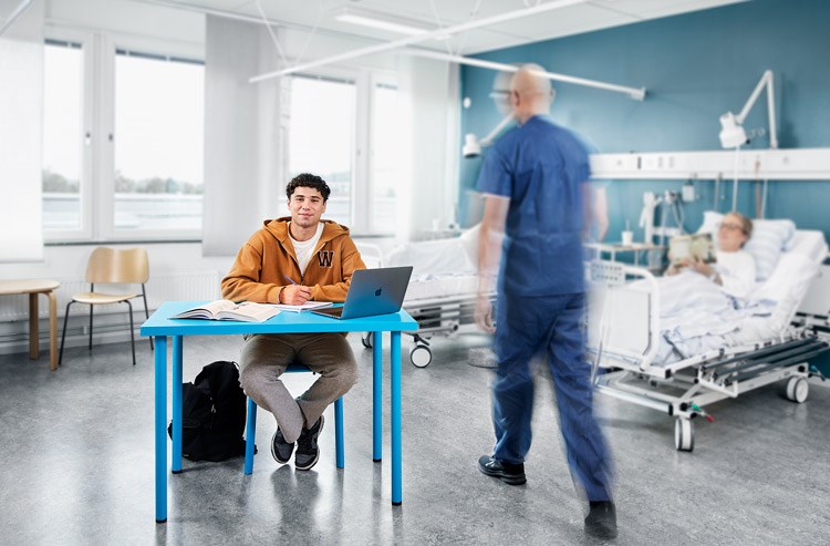 Student som sitter vid en blå bänk i en sjukhusmiljö