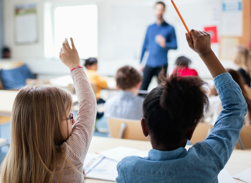 Elever räcker upp handen i klassrummet.